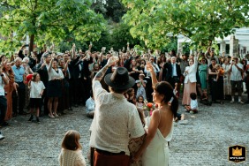 At Quinta da Eira in Penafiel, Portugal, the newlyweds stand with their backs to the camera as a joyful crowd of guests forms a circle around them, raising their glasses in a celebratory toast to the couple’s happiness.